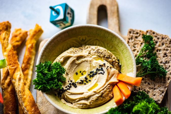 Creamy hummus dip in bowl on cutting board served with veggies and crackers