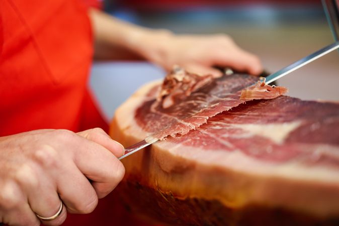 Close up of woman’s hands in butcher shop slicing ham