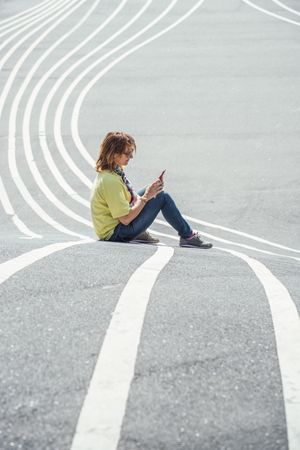 Modern relaxed woman on marked road and browsing smartphone