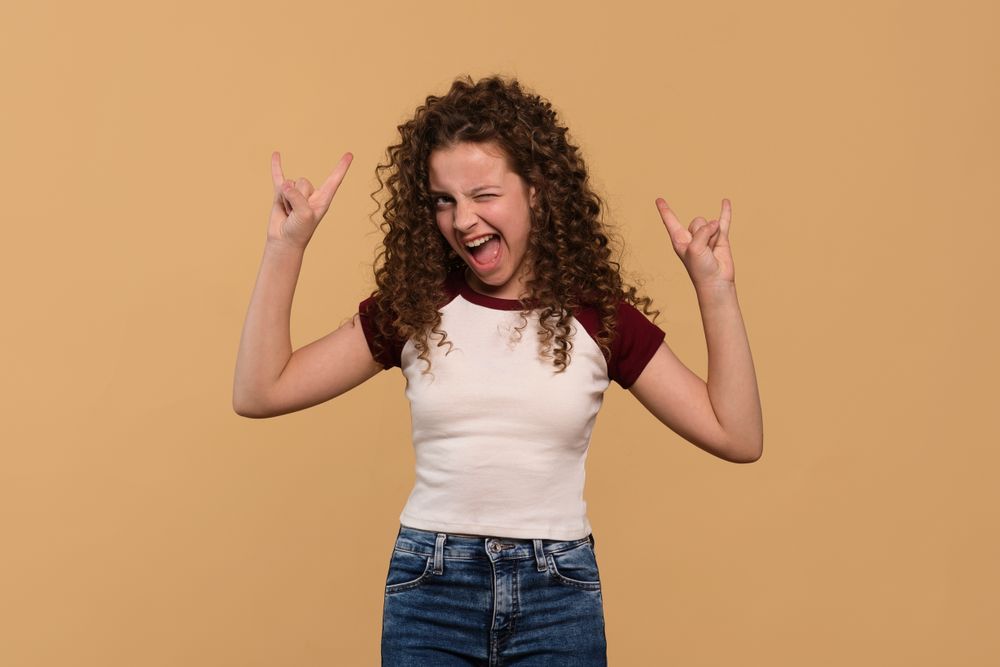 Young girl flashing rock hand signs with enthusiastic expression