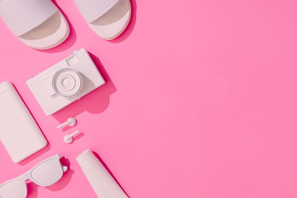 Summer objects of sunglasses, camera, smart phone and sunscreen, EarPods on pink background