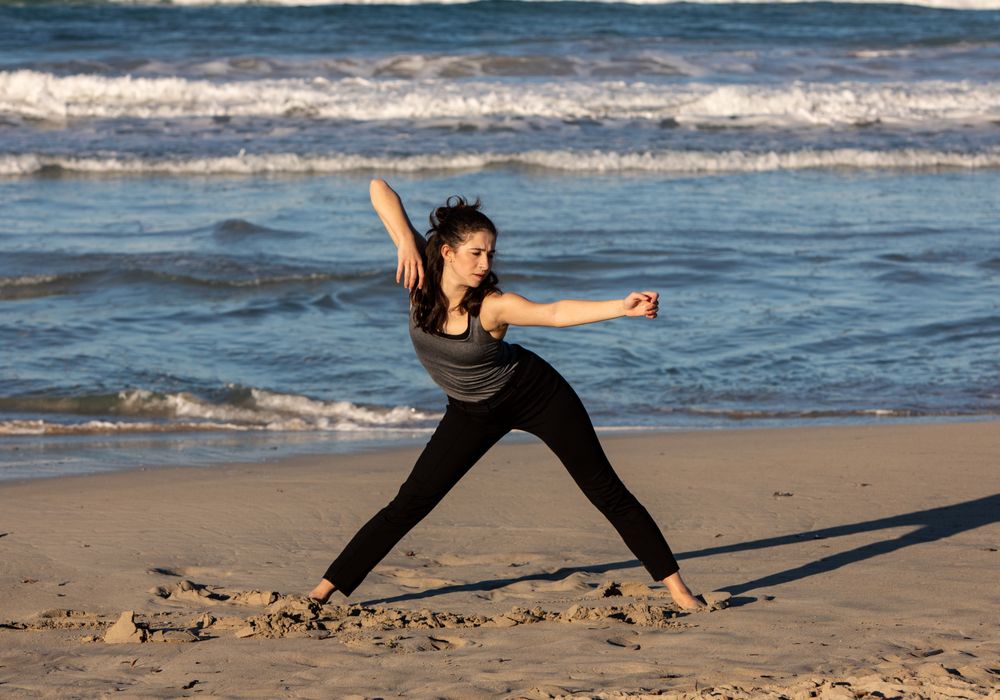Young woman dancing and posing near water on shore