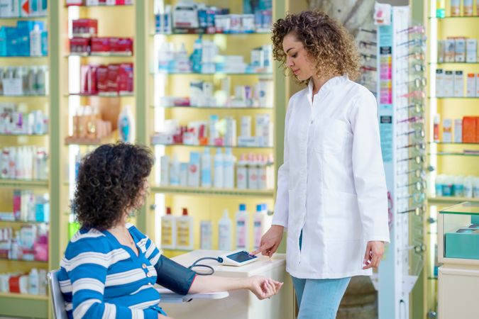 Female pharmacist checking blood pressure of older female in pharmacy