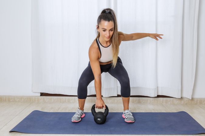 Young woman doing legs workout using kettlebell