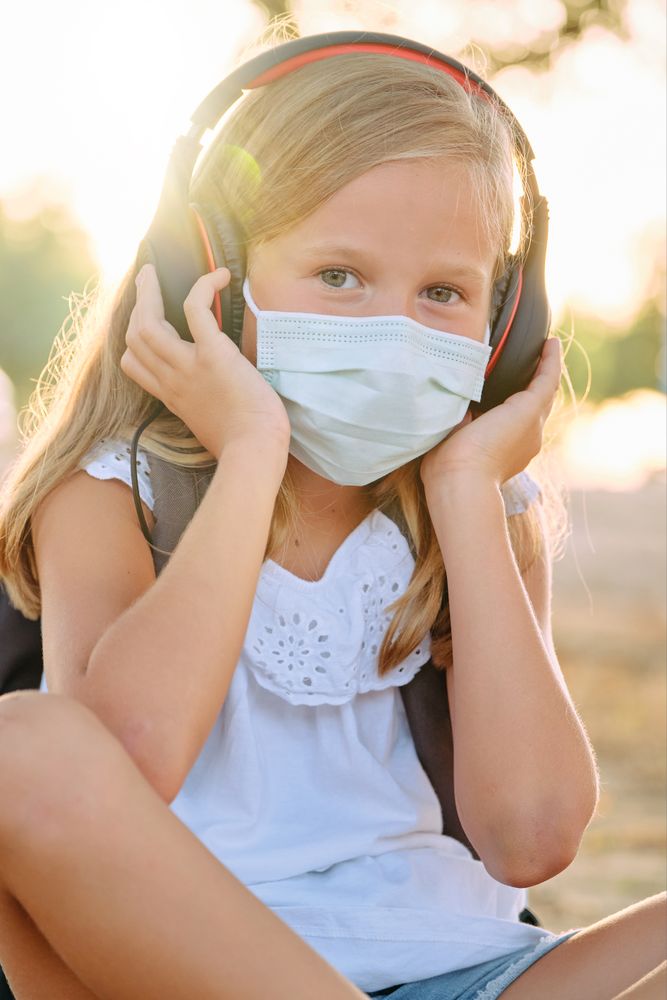 Adorable girl in protective mask and headphones