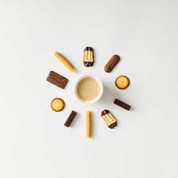 Coffee cup surrounded with cookies on light background