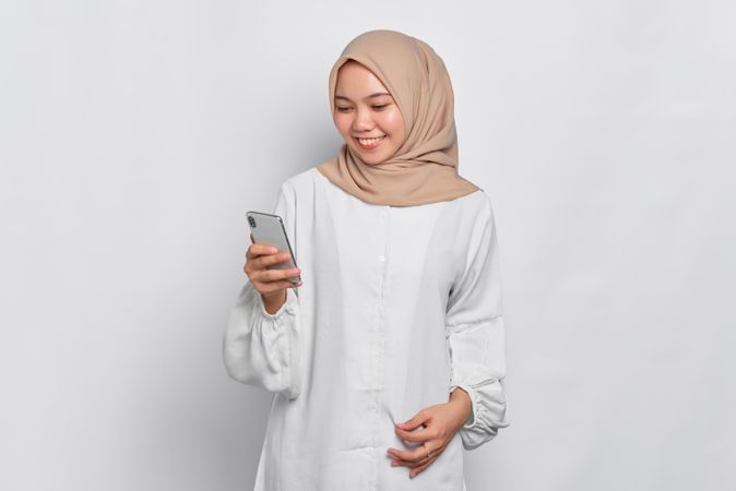 Asian female in headscarf looking happy while looking at her cell phone