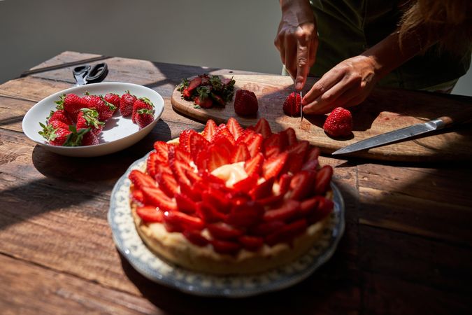Crop chef decorating cake with strawberries on table