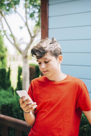 Serious teenage boy standing outside wearing red t-shirt using phone