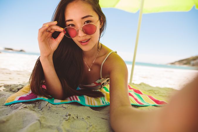 Young woman lying on beach on a sunny day taking a selfie