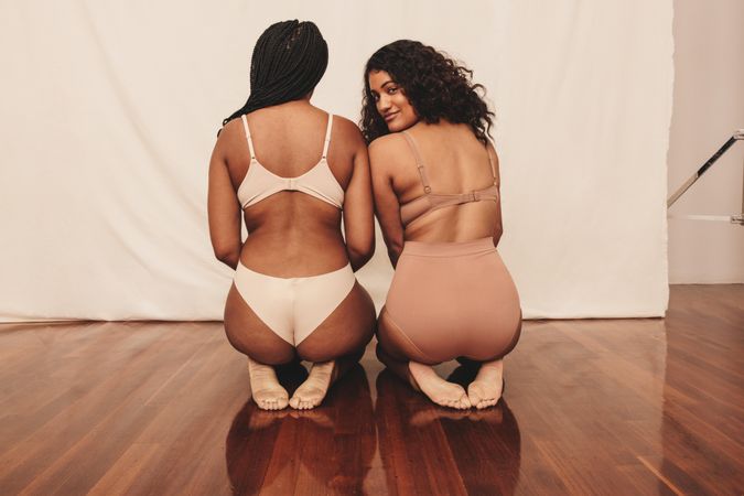 Two confident young women kneeling in underwear in studio photoshoot
