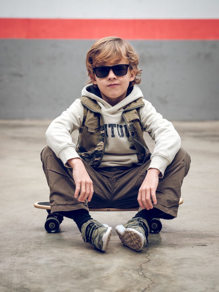 Boy in trendy outfit sitting on skateboard