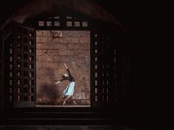 Female ballet dancer dancing in dark passage near stone wall
