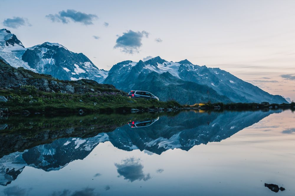 Car on mountain shore with crystal lake reflecting cloudy sky