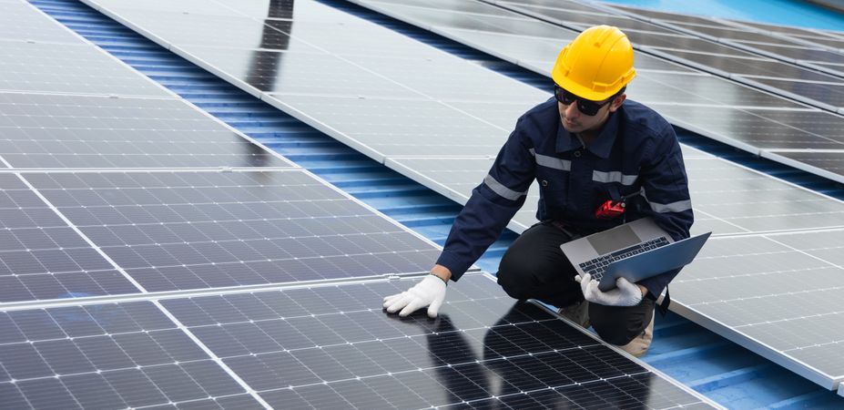 Engineer checking solar cell  or photovoltaic cell by computer laptop installed on the roof of the factory. Technician worker repair or inspect the system. Industrial renewable energy concept
