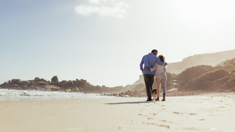 Loving mature couple strolling on near the shore with dog