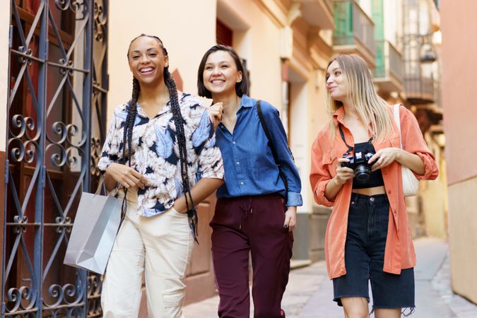 Three happy women walking down narrow lane taking photos