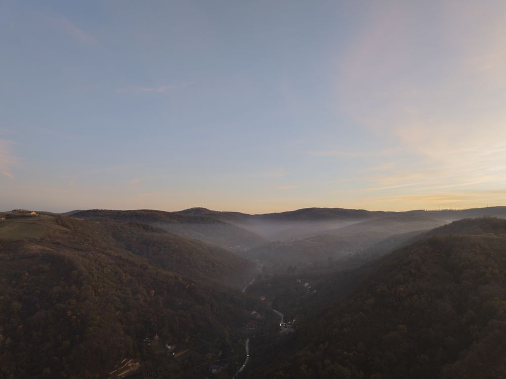 Sunrise Over Forested Hills and Winding Road in Misty Valley.