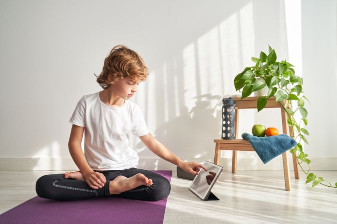 Focused preteen boy sitting in Lotus pose and browsing tablet