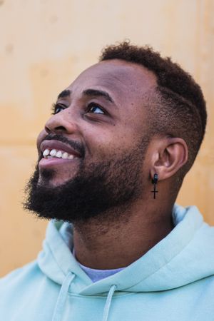 Cheerful Black man in hoodie standing near wall