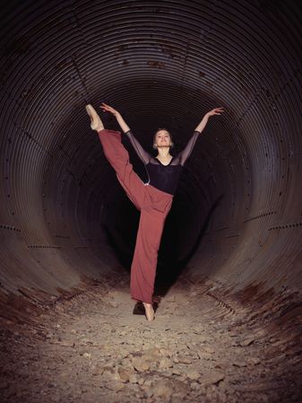 Graceful woman dancing in darkness of underground tunnel