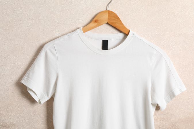 Hanger with blank plain t-shirt on light brown background, space for text