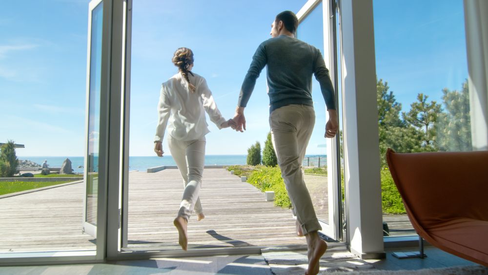 Happy Young Couple Holding Hands  Runs out of Their Home onto the Terrace with the Seaside View.