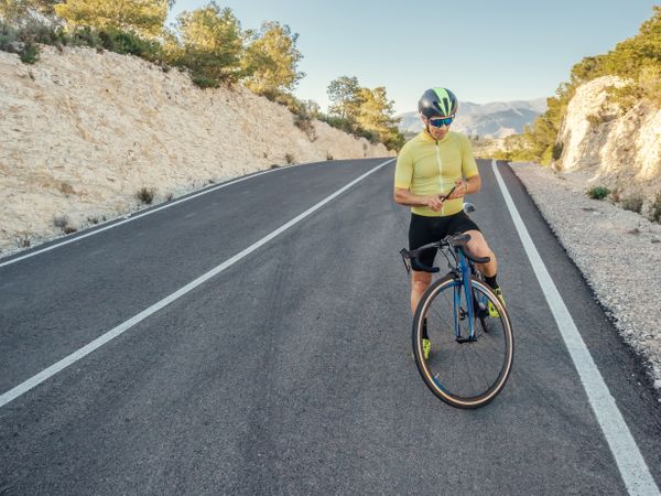 healthy man with smartphone after cycling in a mountain road in a sunny day