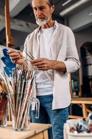 Man with grey beard choosing which paint brush to use, vertical