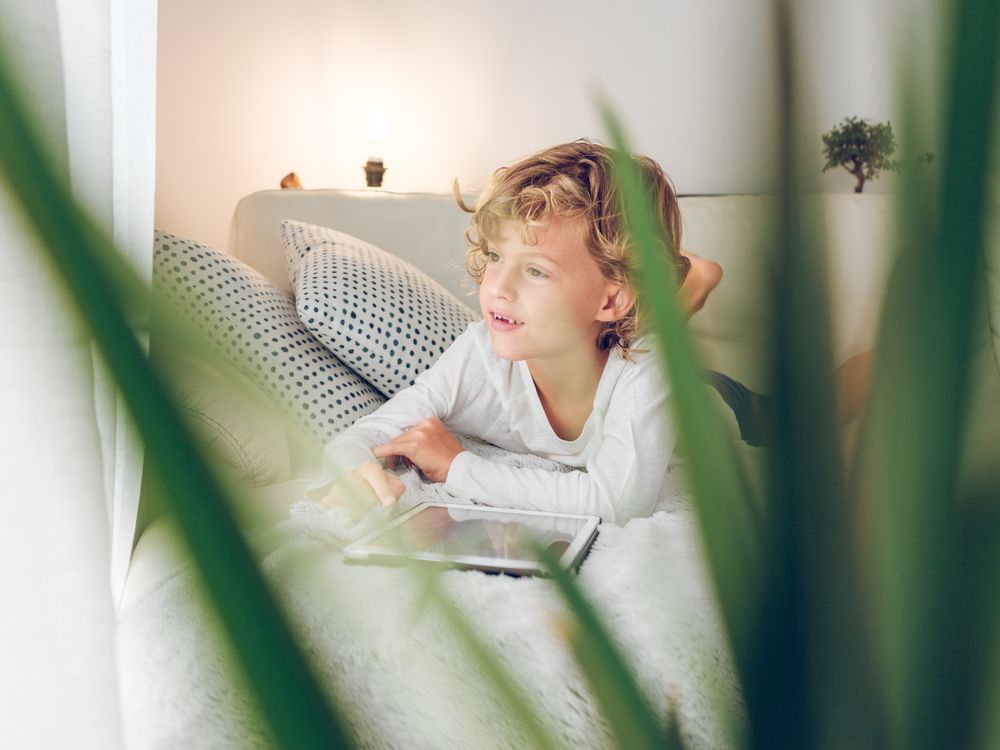 Cute boy on sofa with tablet looking at window