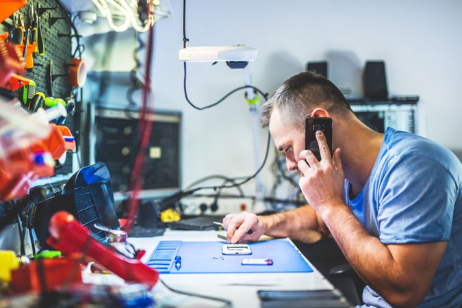 Man talking on phone and repairing smartphone at workplace
