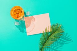 Tropical cocktail with ice cubes, palm leaf  and pink paper card note on vivid blue background