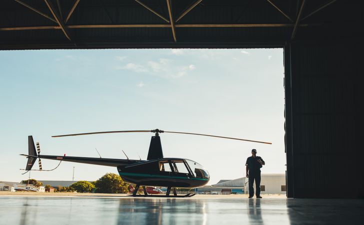 Man walking into a hangar with helicopter parked outside
