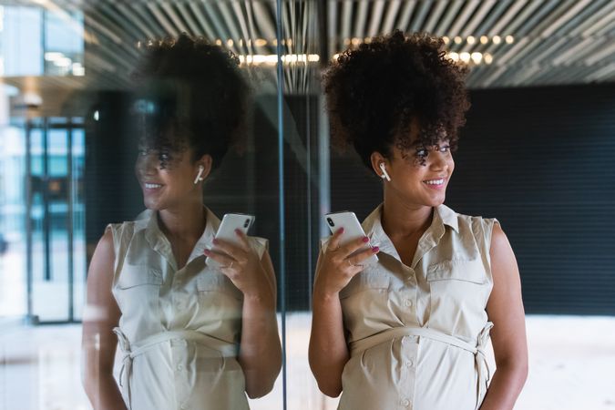 Smiling Black pregnant woman using smartphone and wireless earphones