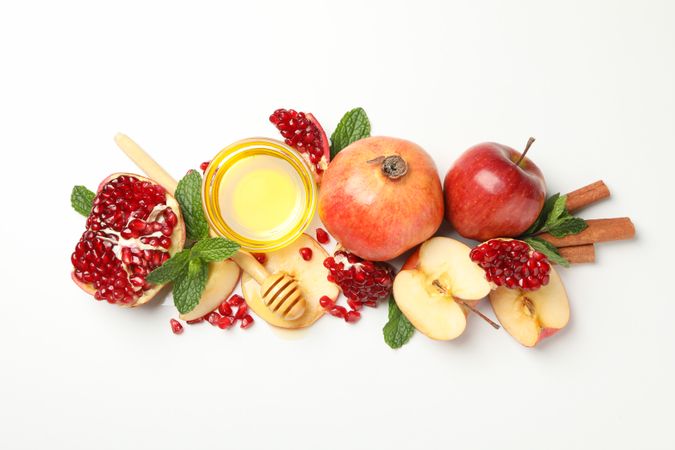Pomegranate, apple quarters, honey in row on blank background