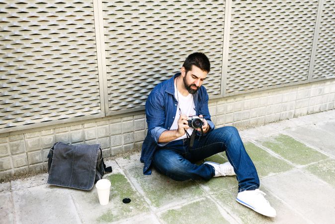 Man checking phone while sitting on pavement outside