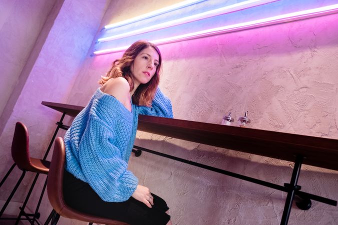 Positive woman with cup at table near wall with neon lamps