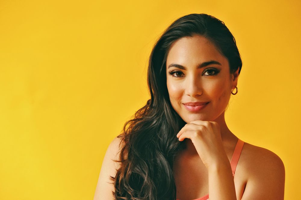 Headshot of calm Hispanic woman looking at camera in yellow room, copy space