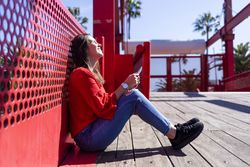Side view of happy woman in red sitting talking on mobile phone outdoors on a bright day