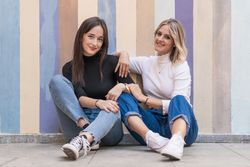 Happy girlfriends sitting against painted urban wall