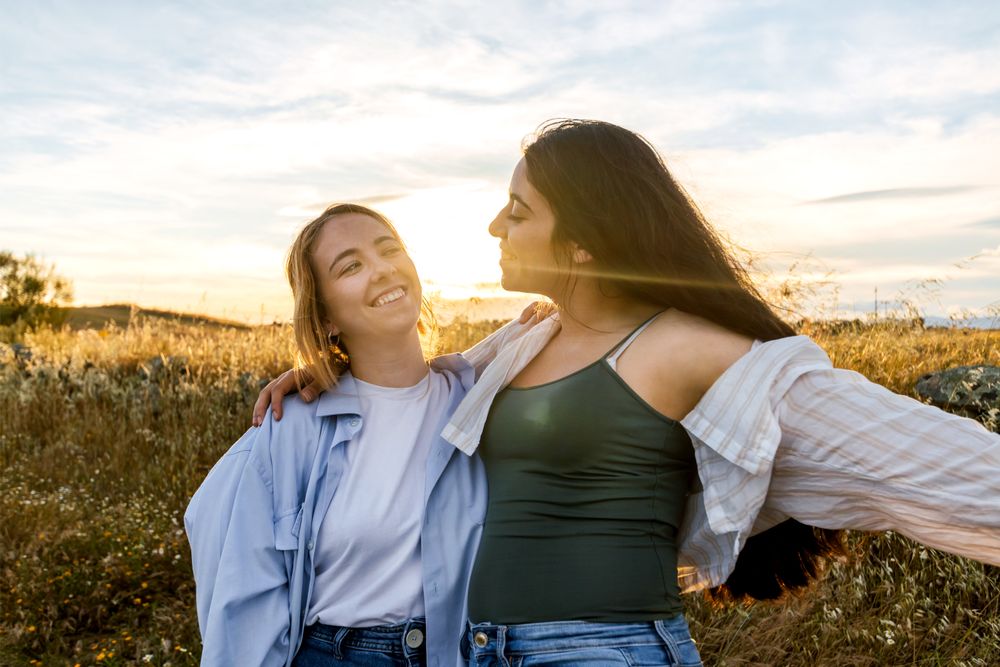 two young women looking each other on a field during sunset