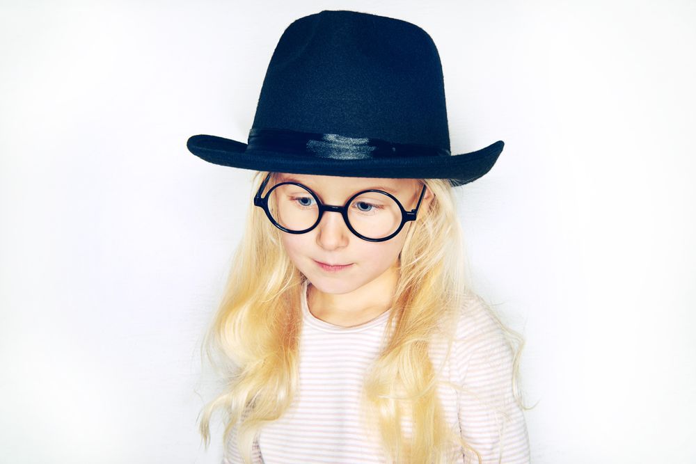 Serious blonde girl looking down wearing hat and glasses