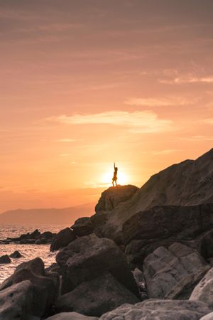 Silhouette of person standing on rock formation near seashore during sunset