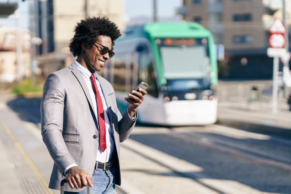Man in jeans and dress shirt with tie looking at phone at train station