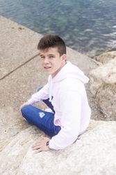 Young male teenager walking along rocky breakwater and looking up at camera