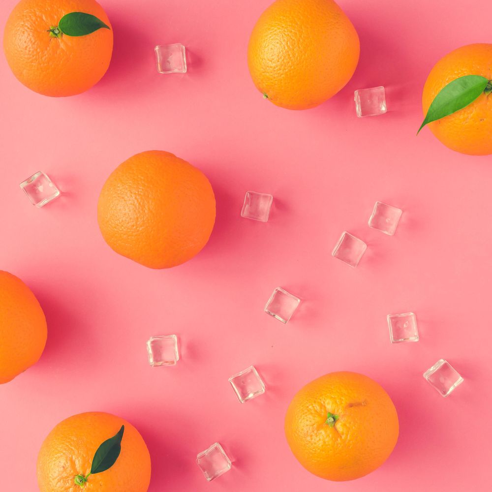 Whole oranges, and ice cubes on vivid pink background