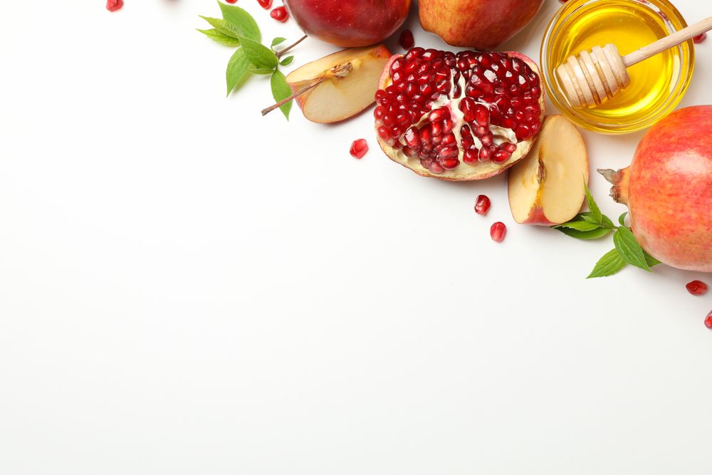 Top view of pomegranate with apples, honey and mint leaves in corner with copy space