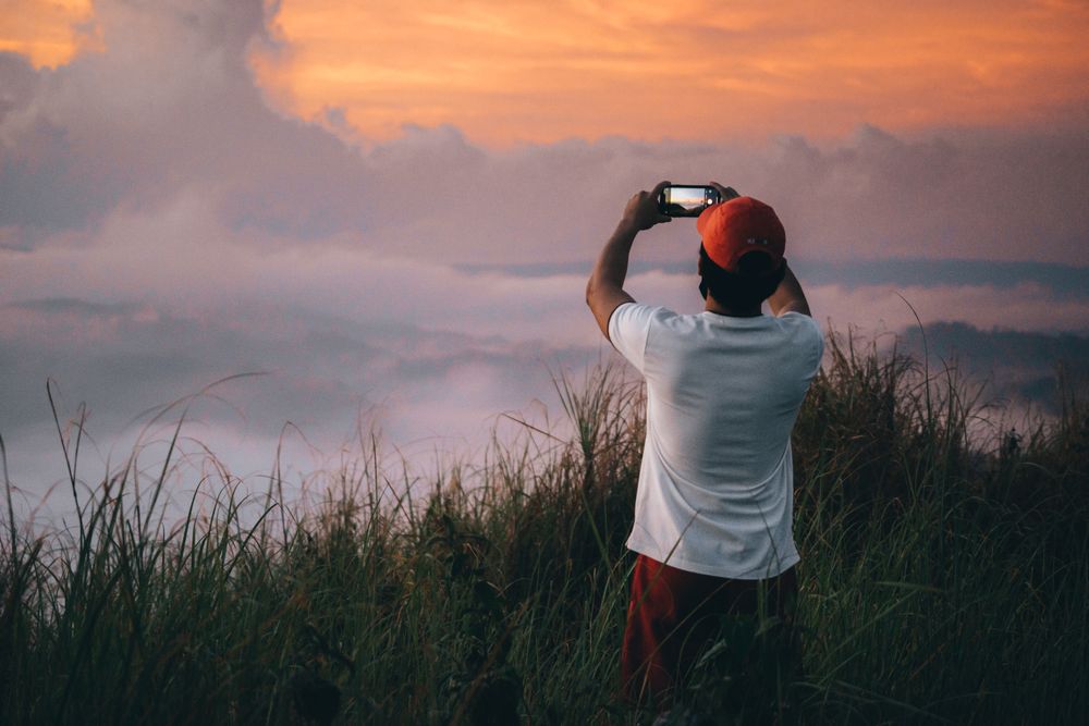 Back view of man standing on highland taking photo of the sunset horizon above the cloud