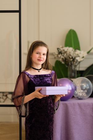 Girl holding gift box and smiling at birthday party.