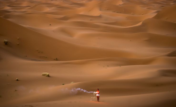 Happy woman holding firework in desert